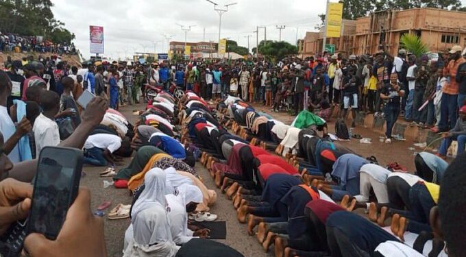 Christian protesters protect their Muslim counterparts as they observe their prayers on the road in Jos